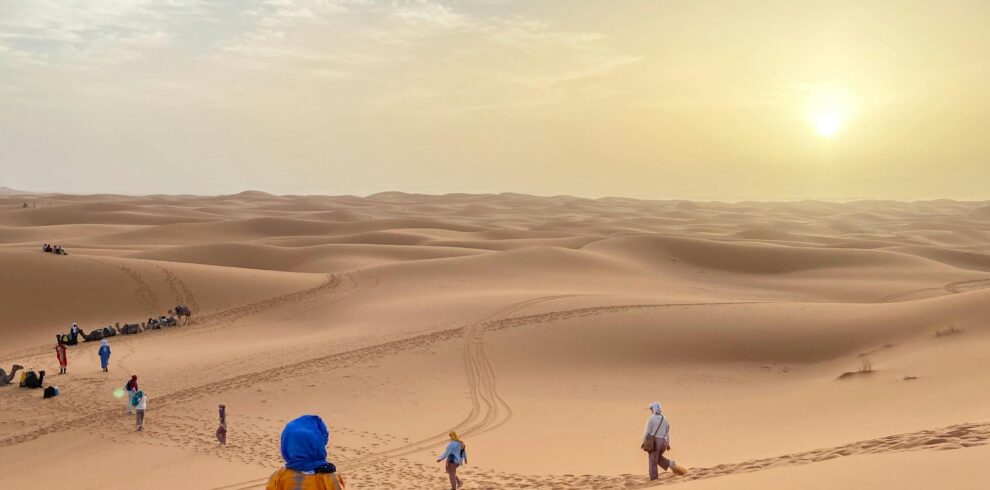Travelers walking through the vast dunes of Merzouga Desert during a stunning sunset in Morocco.
